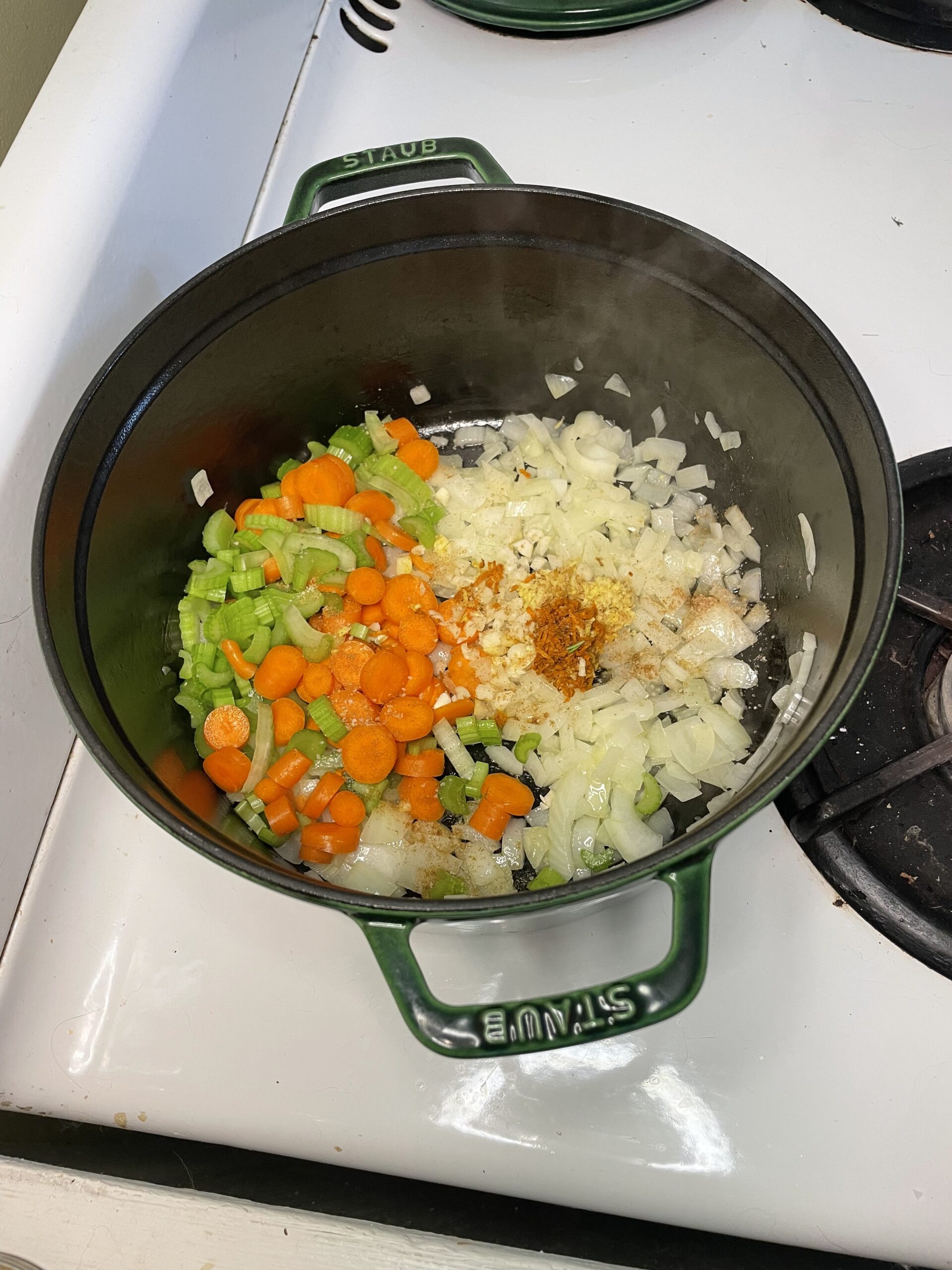 Preparation step of soup-making in a Staub pot, showcasing freshly diced carrots, celery, onions, garlic, and spices arranged for sautéing.
