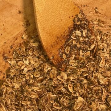 Wooden spoon mixing toasted oats and seeds for homemade maple seeded granola recipe.