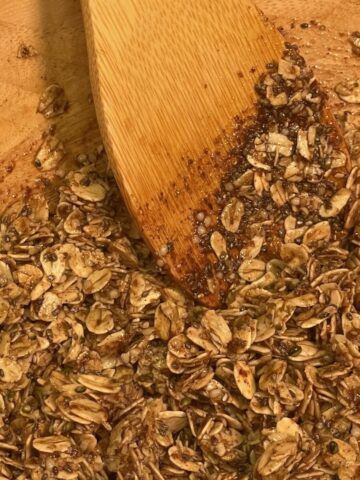 Wooden spoon mixing toasted oats and seeds for homemade maple seeded granola recipe.