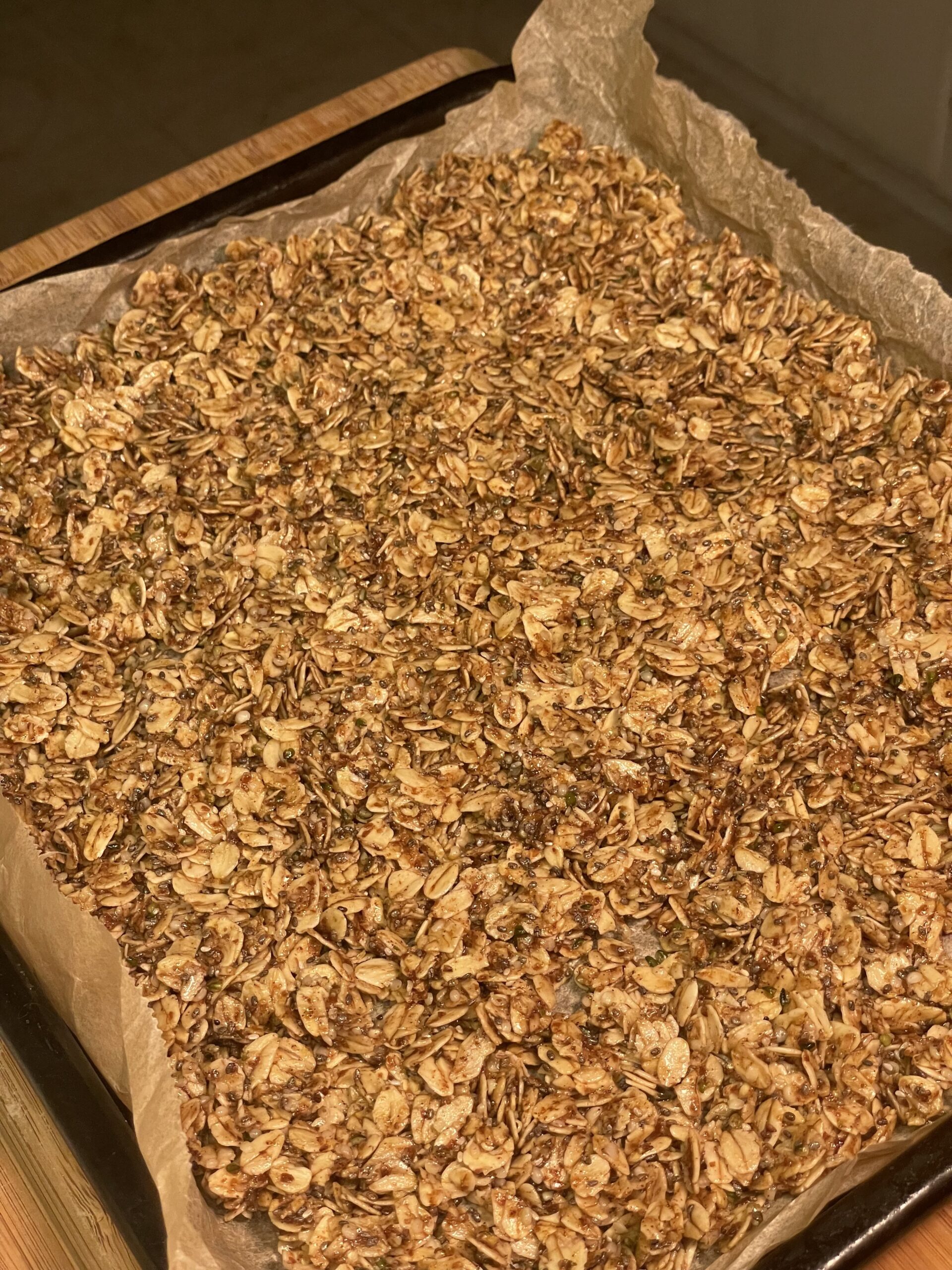 Freshly baked maple seeded granola cooling on a parchment-lined baking tray.