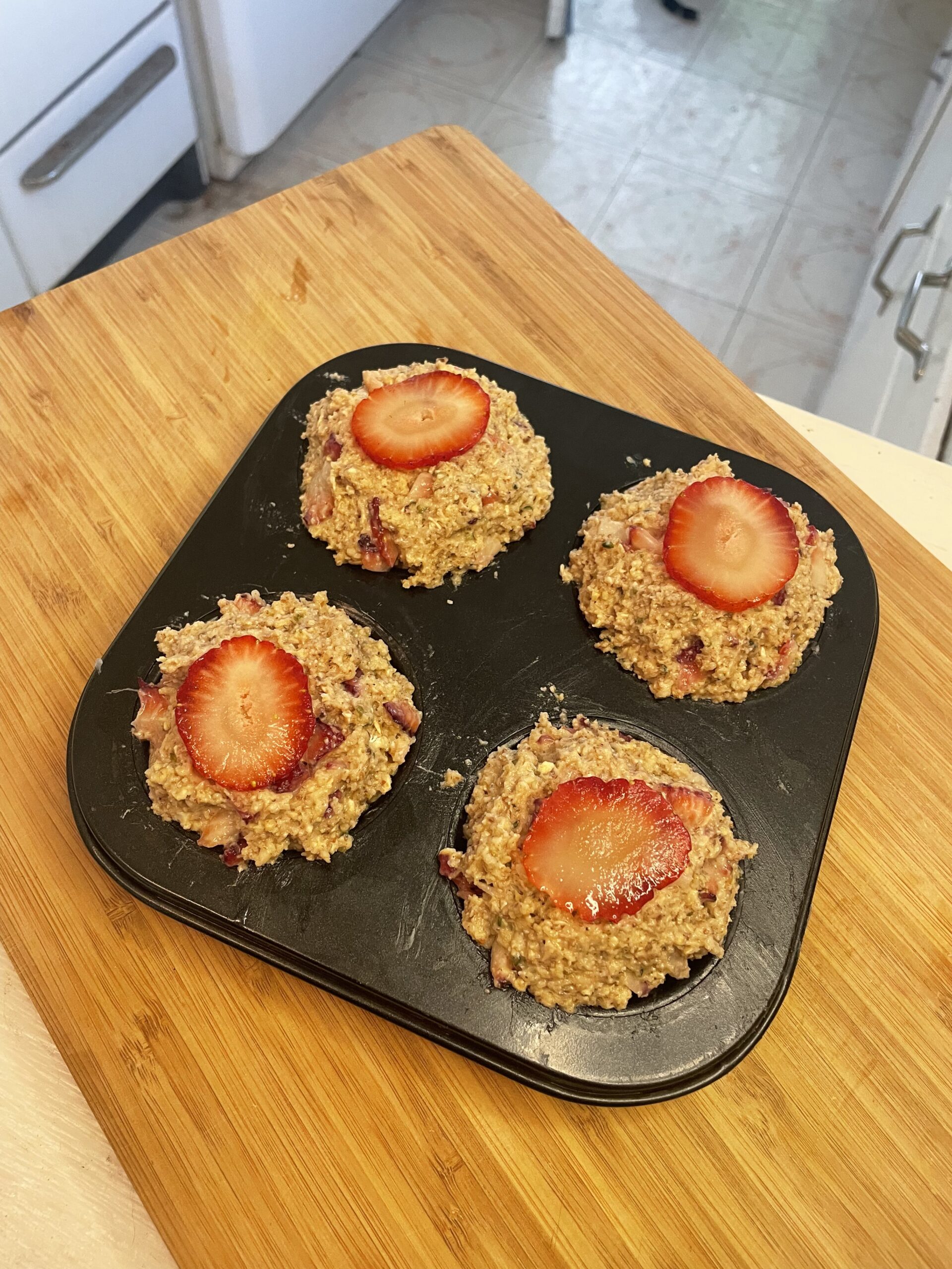 Close-up of unbaked strawberry muffins in a muffin tin, showcasing the coarse oat texture and vibrant strawberry slices on top.