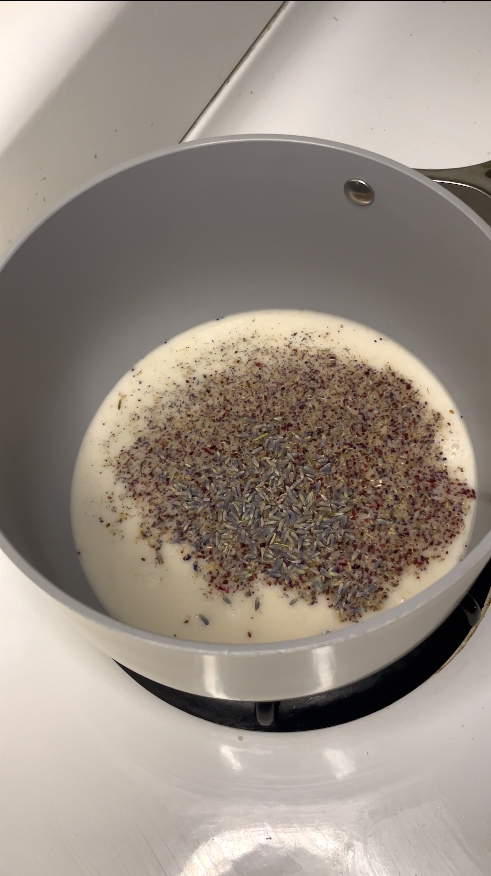 A saucepan with cream and dried lavender buds and chamomile, heating on the stove, suggesting the start of a floral-infused recipe component.