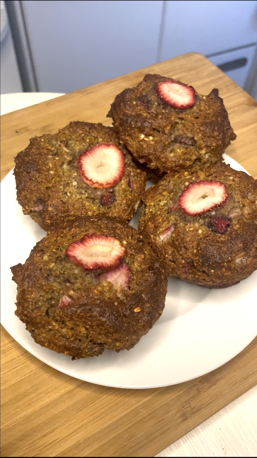 Four golden-brown strawberry muffins arranged on a white plate, each topped with a roasted slice of strawberry, ready to serve.