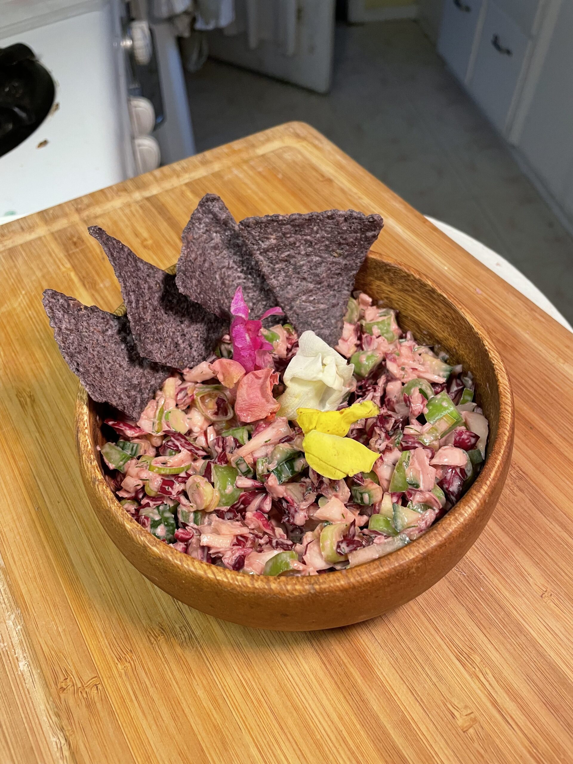 Close-up of crunchy spring slaw with radicchio, celery, cucumber, and edible flowers, served with blue corn chips in a wooden bowl