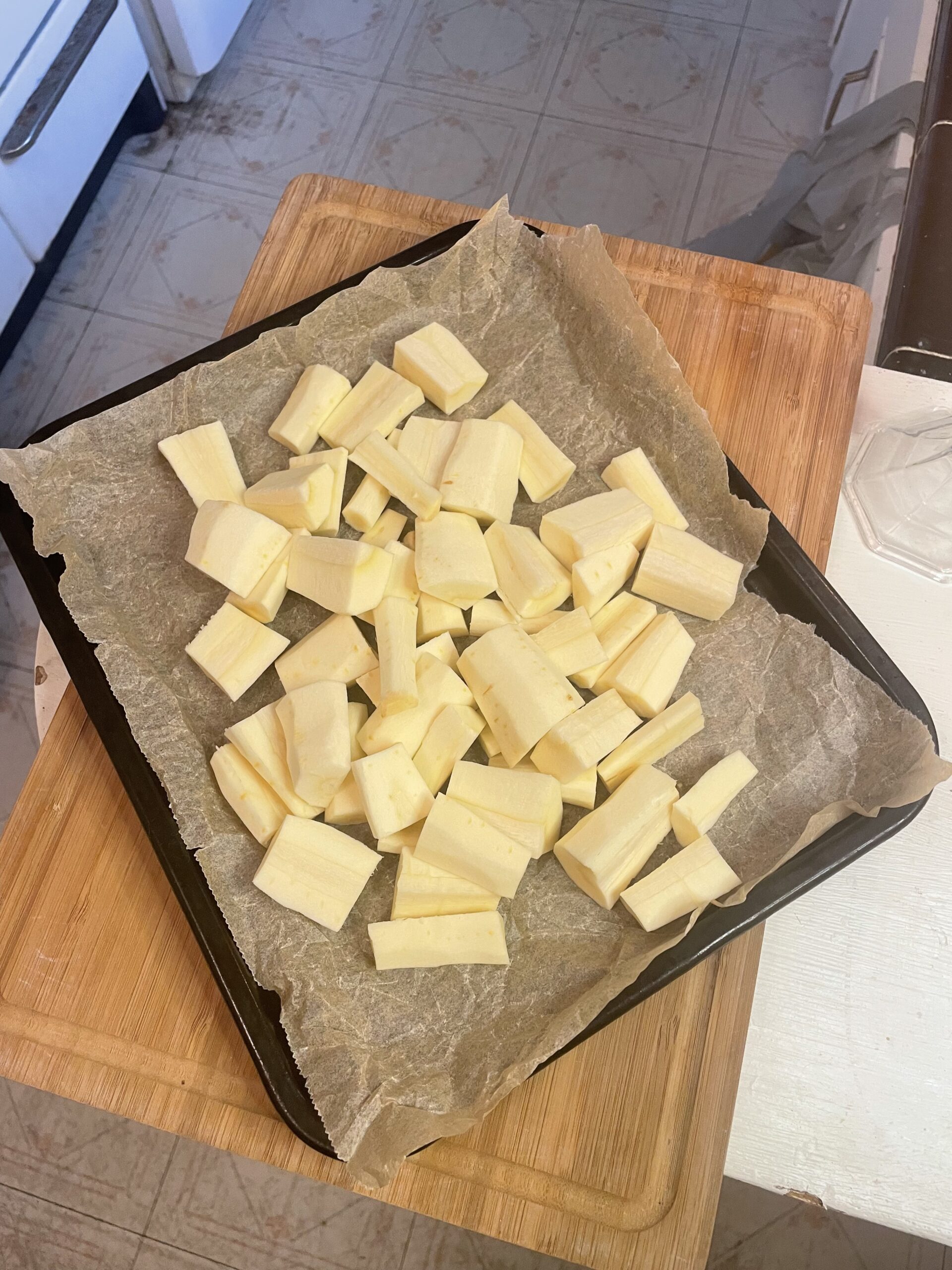 Peeled and chopped raw parsnip pieces arranged on a parchment-lined baking tray, ready for roasting.