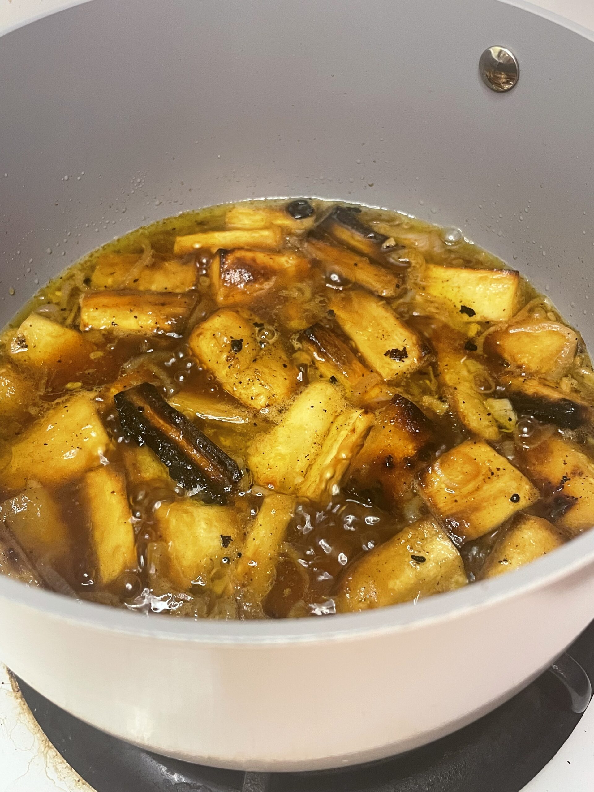 Chunks of roasted parsnip simmering in a pot of seasoned broth, with herbs and spices visible in the bubbling liquid.
