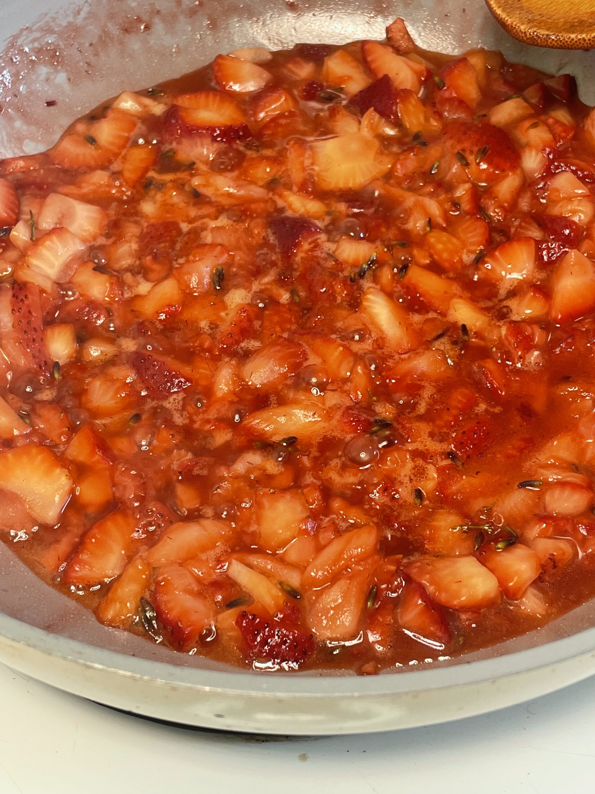 A saucepan filled with chopped strawberries simmering into a glossy compote, with visible herbs suggesting lavender infusion.