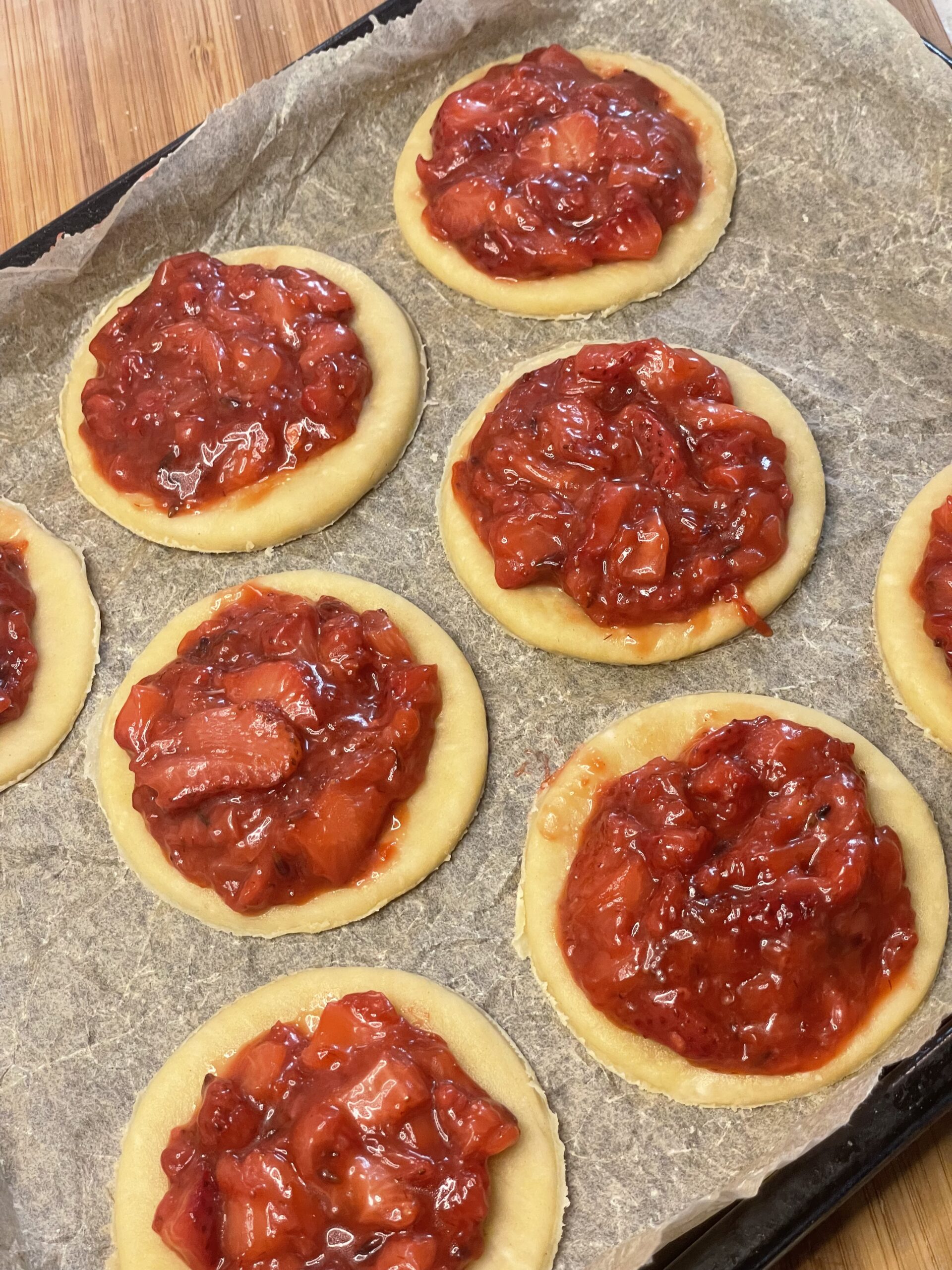 Circular pie crusts laid out on parchment paper, each topped with a generous scoop of strawberry lavender filling.