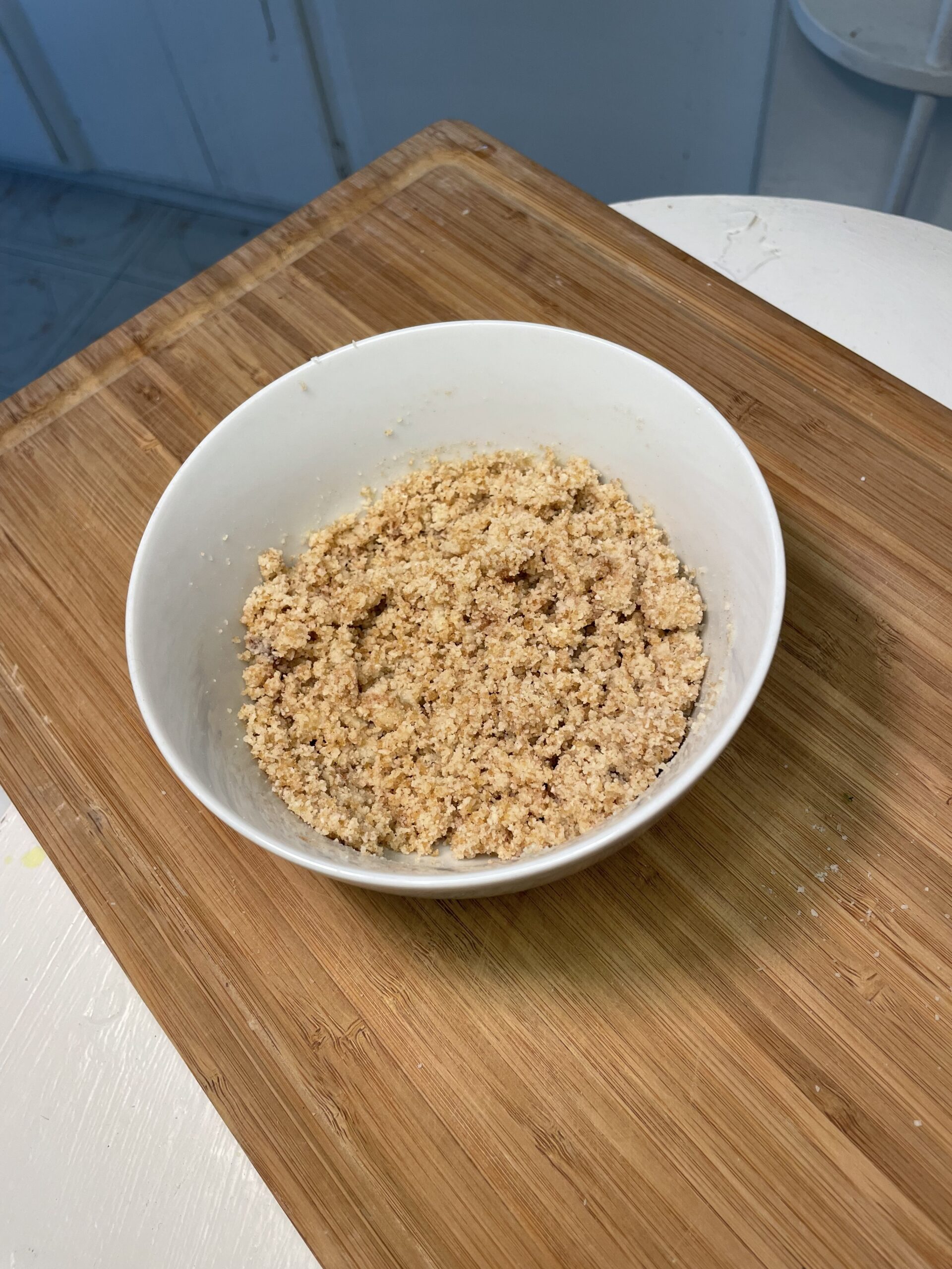 This is a white mixing bowl containing a coffee crumble mixture which will be used to make the final product a streusel. The crumble appears to include almond flour, ground cinnamon, coconut oil, and maple syrup.  The consistency looks soft and crumbly - almost sand like.  
