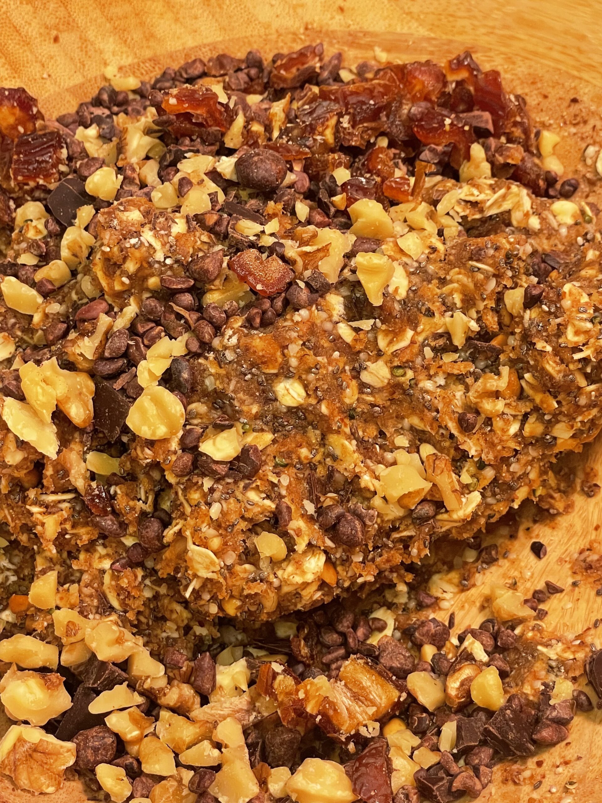 A mixture of cocoa nibs, almond flour, chia and hemp seeds, chopped nuts and dried fruit in mixed together in a large bowl.