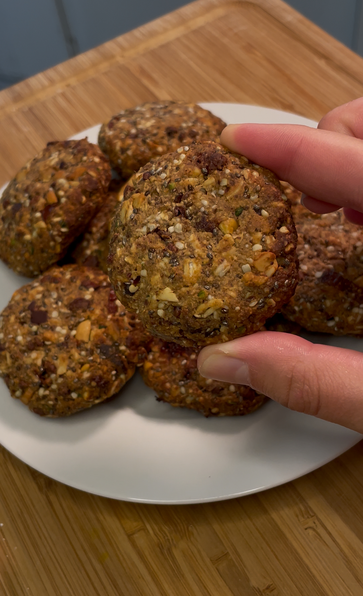 A white plate stacked with Wander Witch Cookies rests on a wooden kitchen countertop.  A person is holding one of the cookies close to the camera to demonstrate what they look like close up.