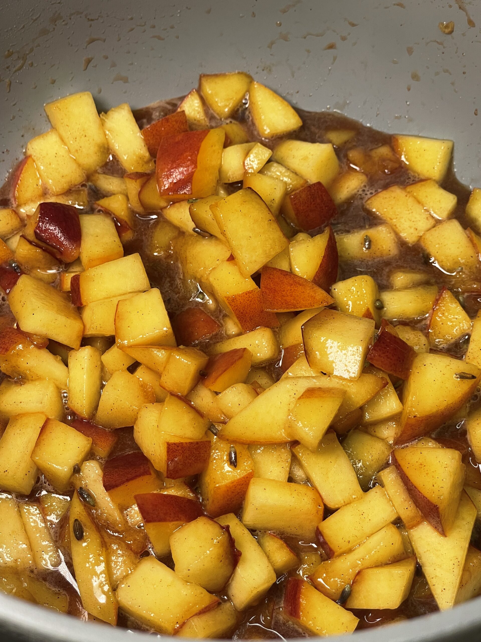 Small cut pieces of fresh peaches dressed in a brown sugary syrup cooking in a grey pan. 