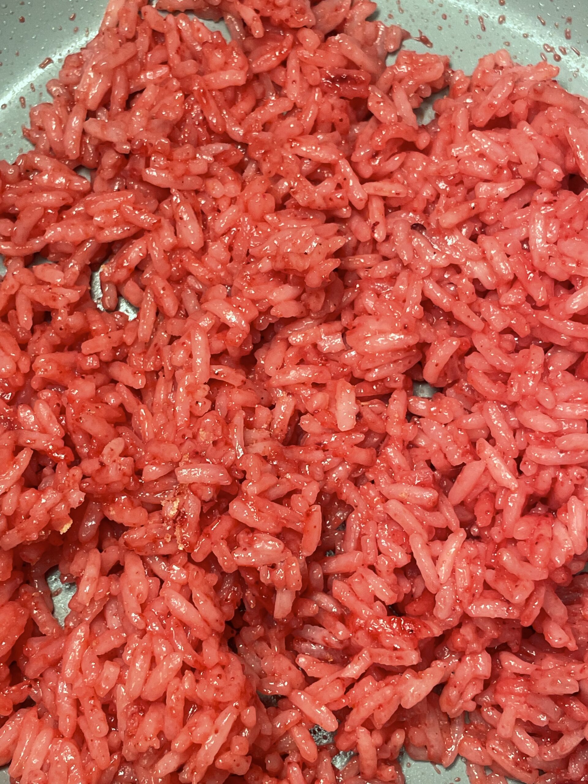 In a grey pan, pink colored rice is cooking. 